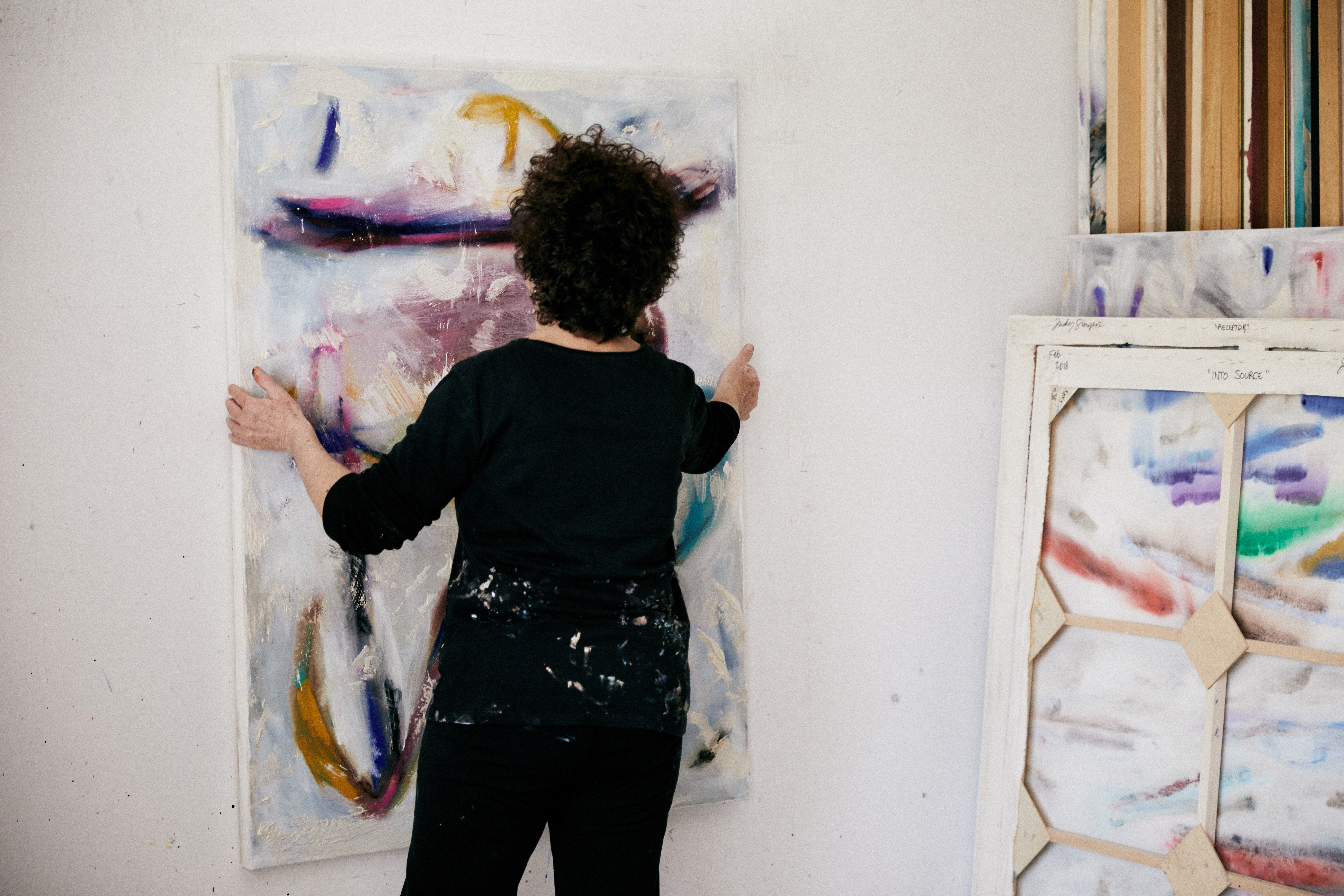 Judy Singer, art entrepreneur, hanging one of her paintings on a wall